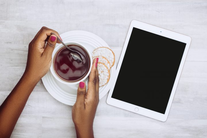 Lady stirring a cup of tea with her iPad on the side.